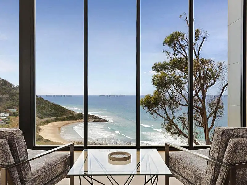Two chairs and a side table sitting in front of glass wall with ocean views at Iluka Blue a luxury holiday house on the Great Ocean Road in Victoria Australia. 