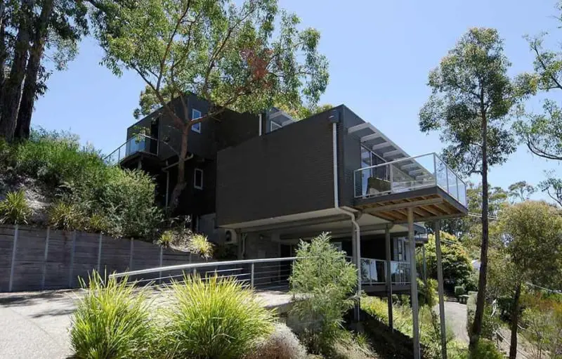 Side view of the Lorne Luxury holiday house surrounded by trees on a clear blue day.