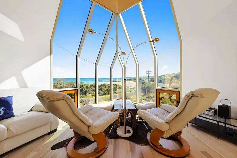 Sitting area with lounge chairs and a large oblong shaped window with ocean views at Manta Ray One in Apollo Bay.