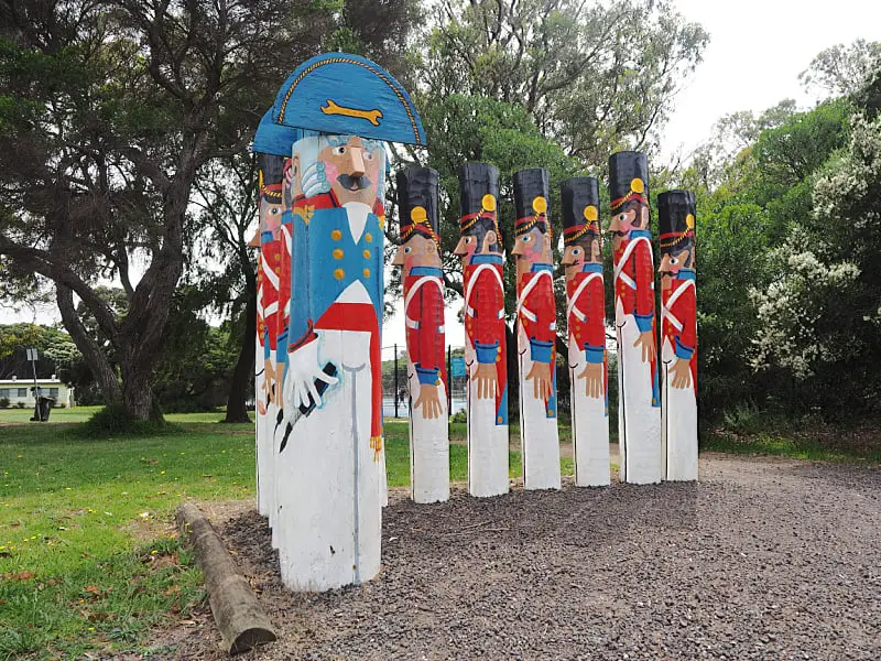 A collection of colorful bollard sculptures resembling soldiers and an admiral in traditional naval uniforms, standing in a Barwon Heads park with trees in the background.
