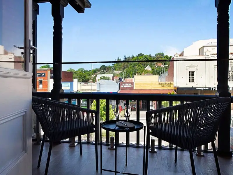 Inviting balcony view from 1913 On Vincent accommodation in Daylesford, showcasing comfortable black seating and a quaint table set against the picturesque backdrop of Daylesford's lush hills and local architecture.