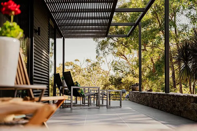 A serene patio area at Bohemia accommodation in Daylesford, featuring modern outdoor furniture and a slatted roof design, set against a backdrop of lush Australian bushland.