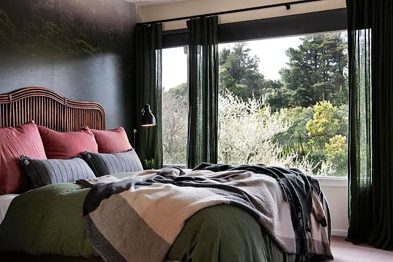 Elegant bedroom inside the Treehouse Spa Villa in Daylesford, featuring a rattan headboard, plush bedding in earthy tones, and large windows offering a panoramic view of the tranquil forest.